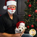 Man with a cloth face mask and a small dog wearing a Santa hat