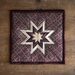 Isolated image of the Plumberry Folded Star Squared Hot Pad on a wood table