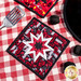 The black and red Peace, Love & BBQ Folded Star Squared Hot Pad on a red checkered picnic table
