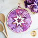 pink and purple variegated circular hot pad on a white marble countertop with a wooden spoon and purple flowers