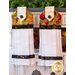 Two white hanging towels with rich earth toned patterns, one grape themed and one pomegranate themed