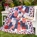 Quilt filled with red white and blue patriotic imagery draped over white out-door furniture.