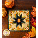 square hot pad with leaf pattern and cream background featuring a central folded star design, on wood table.