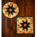 Two hot pads with leaf pattern and cream background featuring a central folded star design, on wood table.