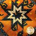 Orange Halloween themed hot pad with central folded star on wood table.