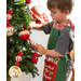 Photo of a child wearing the Peppermint Candy apron decorating a Christmas Tree, with the Santa's Little Helper bag in the background