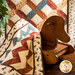 Small earth toned cowboy themed quilt draped over rocking horse with larger matching quilt hanging in the background.