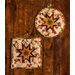 Two hot pads with autumn leaf motifs and central folded star design made with cream fabrics sitting on wood table.