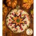 hot pad with autumn leaf motifs and central folded star design made with cream fabrics sitting on wood table next to pumpkins.