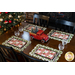 Christmas themed scalloped placemats featuring red trucks, wagons, and pine trees as part of a table setting.
