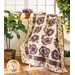 Cream quilt with flowers made of layered purple and green fabric draped over furniture.