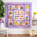 Quilt featuring multicolored watercolor florals on white with purple borders hanging on white paneled wall.