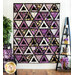 Purple and white quilt with triangle geometric design and floral prints hanging from white panel wall.