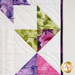 A quilt with geometric square and triangle designs made of multicolor fabrics on white.