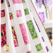 Quilt of squares and rectangles made of pink, purple, and green floral fabrics on white background draped over furniture.