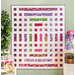 Quilt of squares and rectangles made of pink, purple, and green floral fabrics on white background hanging on green panel wall.