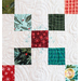squares of holiday fabrics arranged on white quilt.