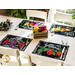 Black placemats with prints of fruits, vegetables, and produce themed phrases set on table with glasses and matching cloth napkins.