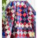 Red, white, and blue quilt of squares in diamond pattern with patriotic themed fabrics draped over furniture.