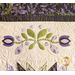 Close-up of a quilt featuring floral appliqué in lavender, green, and black, with intricate stitching.