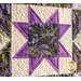 Close-up of a quilt featuring a star pattern in purple and lavender, with intricate stitching.