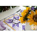 Table runner with geometric design with white and purple lavender and bee themed fabrics on table set with matching napkins.