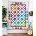 White quilt with multicolor floral and geometric designs hanging on white panel wall.