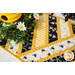 Table runner made of diagonal strips of bee themed fabrics in yellow, black, and white.