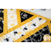 Table runner made of diagonal strips of bee themed fabrics in yellow, black, and white.