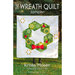 the front of The Wreath Quilt pattern book featuring someone holding the finished quilt in front of them, standing outside in green grass