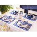 Scalloped placemats made of blue and cream floral printed fabrics arranged on white table also set with plates and napkins.