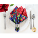 A cloth napkin made with red and blue floral fabrics on a white dinner plate next to silver silverware