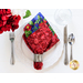 A cloth napkin made with red and blue floral fabrics on a white dinner plate next to silver silverware