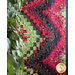 A vibrant quilt with red, green, and black geometric patterns, partially obscured by leafy plants.