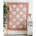 Quilt with red and white floral patterns hanging on a wall, surrounded by greenery and decor.