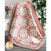 A patterned quilt hangs gracefully, featuring floral designs and pinwheel motifs in soft colors.