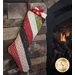 A patchwork Christmas stocking hangs from a stone fireplace next to a glowing fire.