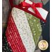 A holiday-themed quilted bag with red, white, green, and black patterns, holding gift cards and tied with a ribbon.