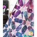 A colorful quilt featuring geometric patterns in purple, blue, and green draped over a chair.