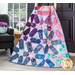 A colorful quilt draped over a chair, featuring triangular patterns in purple, blue, and teal.