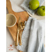 Two fringed cloth napkins on a cutting board with gold silverware and green apples