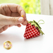 An image of a hand putting a pin in a strawberry pincushion.