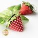 A close-up image of two strawberry pincushions next to a green leaf.