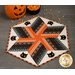 Halloween themed table topper with diamonds made of strips of black and orange fabric on a white background with black cat face appliqué.