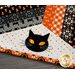 Halloween themed table topper with diamonds made of strips of black and orange fabric on a white background with black cat face appliqué.