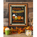 An autumn themed wool wall hanging with applique words, pumpkins, and coffee cups hung on a wooden wall