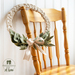 Beige wreath made with a braided design and green leaves made of fabric accented with a beige ribbon hanging from a chair.