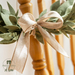 Beige wreath made with a braided design and green leaves made of fabric accented with a beige ribbon, close up on the ribbon.