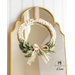 Beige wreath made with a braided design and green leaves made of fabric accented with a beige ribbon hanging from a mirror.