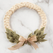 Beige wreath made with a braided design and green leaves made of fabric accented with a beige ribbon on marble background.